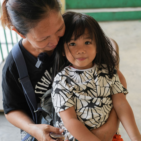 woman with young girl sitting on her lap, girl smiling at camera wearing black and white shirt