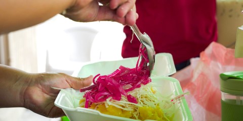 a person serving yucca and cabbage with pickled red onion 