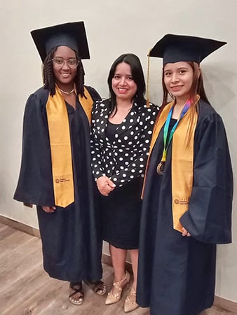 Two young women in graduation gowns with their leader