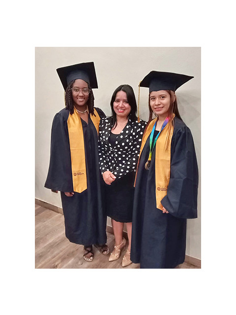 Two young women in graduation gowns with their leader