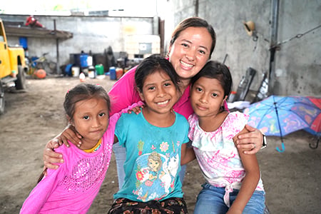 Woman in pink shirt with three Guatemalan girls in their community