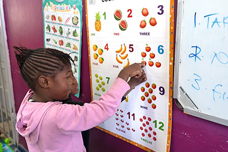 two young children learning counting and pointing at a number poster