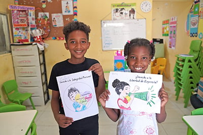 two children in classroom holding coloring pages