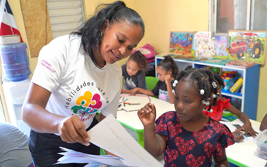 woman in white shirt sitting at a table instructing young students
